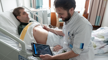 Foto (kleur) arts die ultrasonografie doet bij patiënt op bed